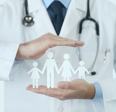 An urgent care doctor holding a paper family consisting of a mother, father, daughter and son holding hands.