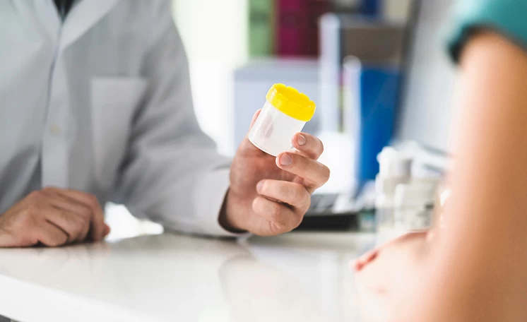 A provider handing a patient a specimen cup for a drug test