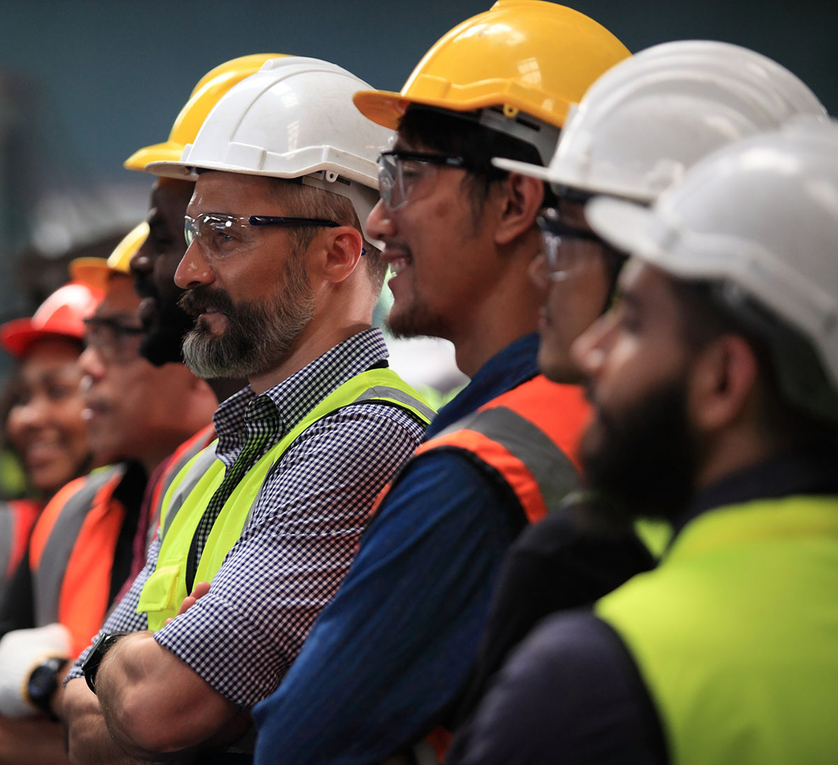 A diverse group of workers in hard hats and safety vests at a workplace meeting