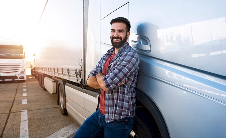 A smiling truck driver standing beside his semi truck